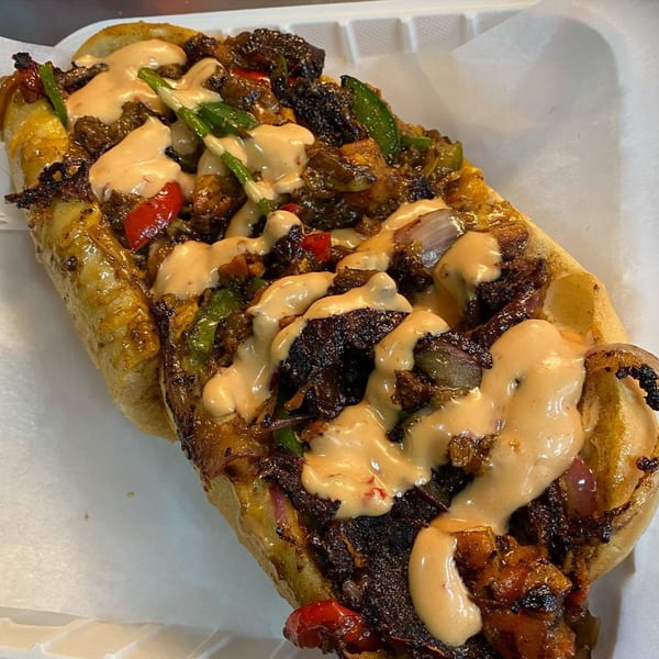 A close-up of an American cheesesteak sandwich, generously topped with sauce, peppers, and onions.