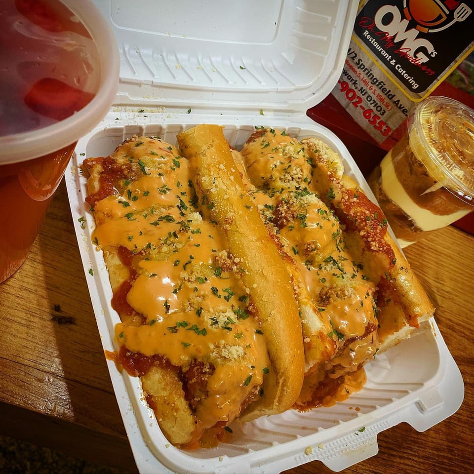 Three meatball subs with orange sauce and parsley, a drink, and a dessert cup from Oh My Goodness.