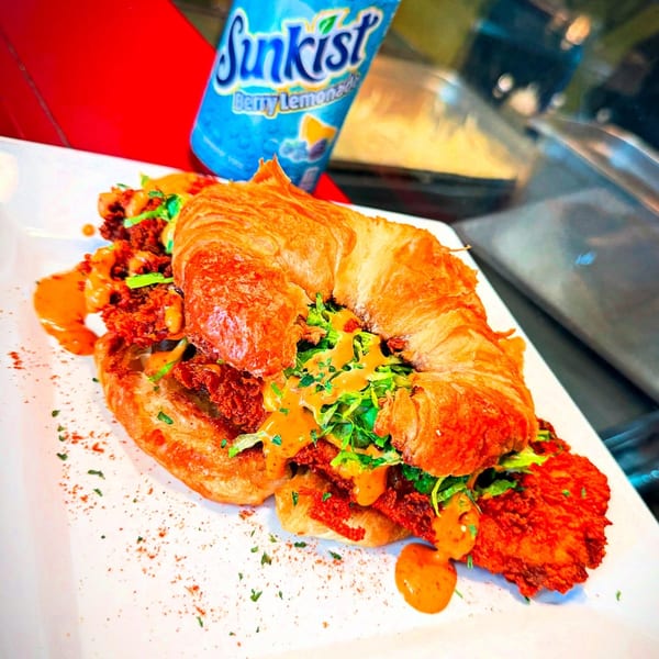 Crispy fried chicken sandwich on a croissant with sauce and lettuce, next to a Sunkist Berry Lemonade.