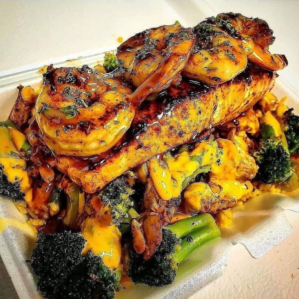 Grilled salmon and shrimp topped with sauce, served with broccoli and corn in a takeout container.
