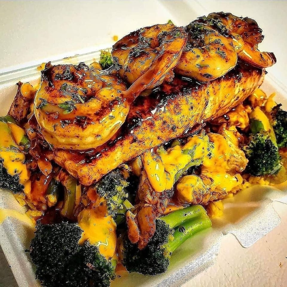 Grilled salmon and shrimp topped with sauce, served with broccoli and corn in a takeout container.