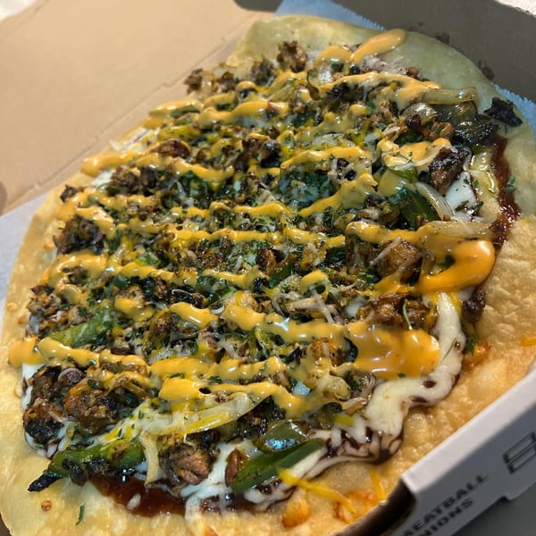 An American flatbread pizza with meat, green peppers, onions, cheese, and a yellow sauce drizzle.
